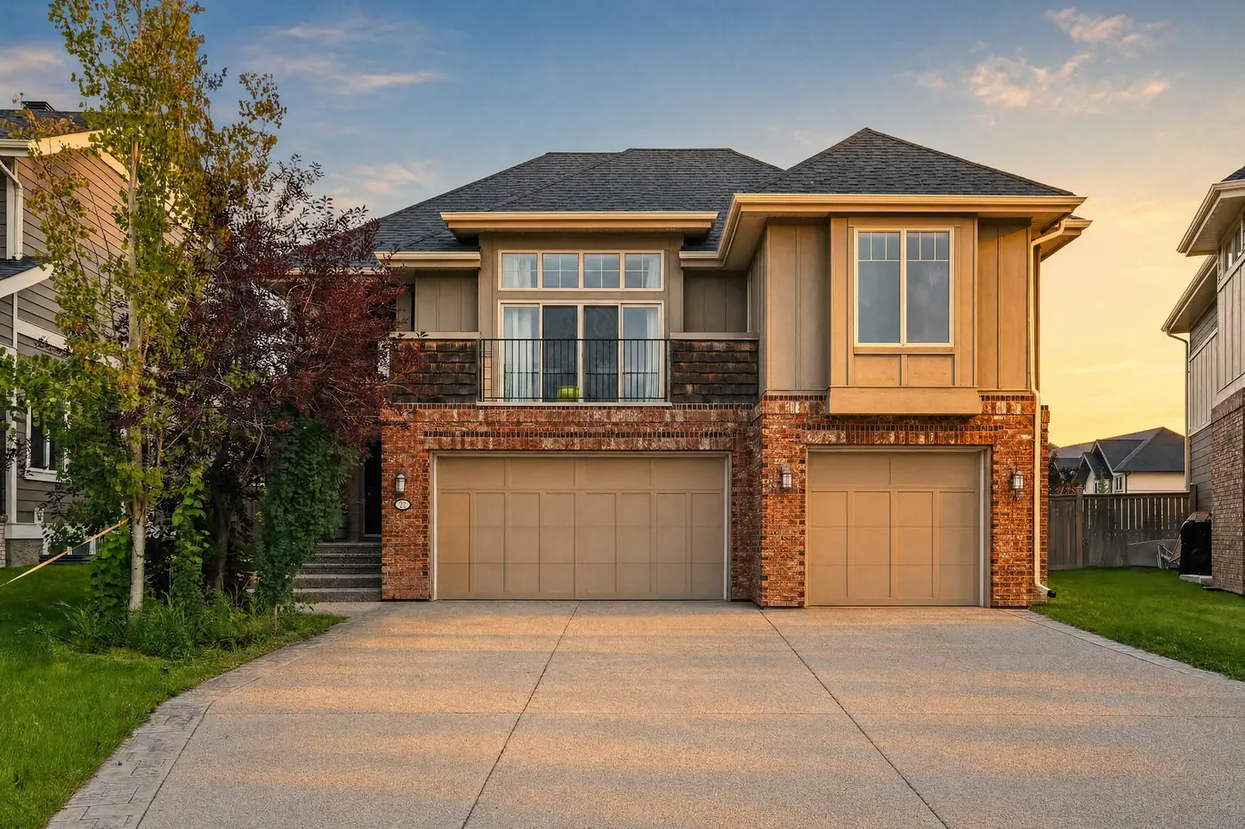 The full front elevation of 22 Wendham Place SW at golden hour — low warm sunlight raking across the red-brick banding and taupe siding, long shadows stretching over the broad exposed-aggregate driveway.