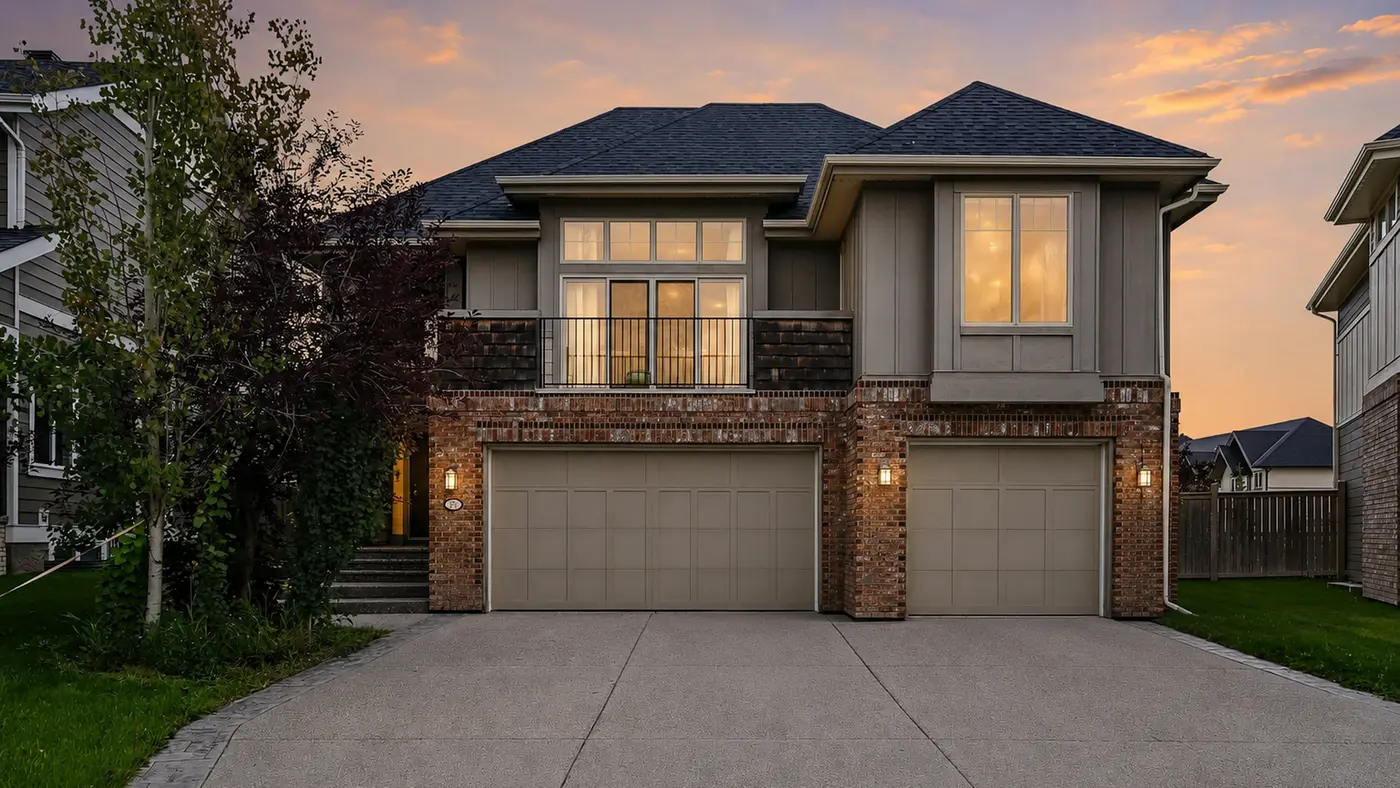 The front of the home at twilight — windows glowing warmly under a peach-and-lavender dusk sky, sconces lit beside the triple garage at the head of the cul-de-sac.