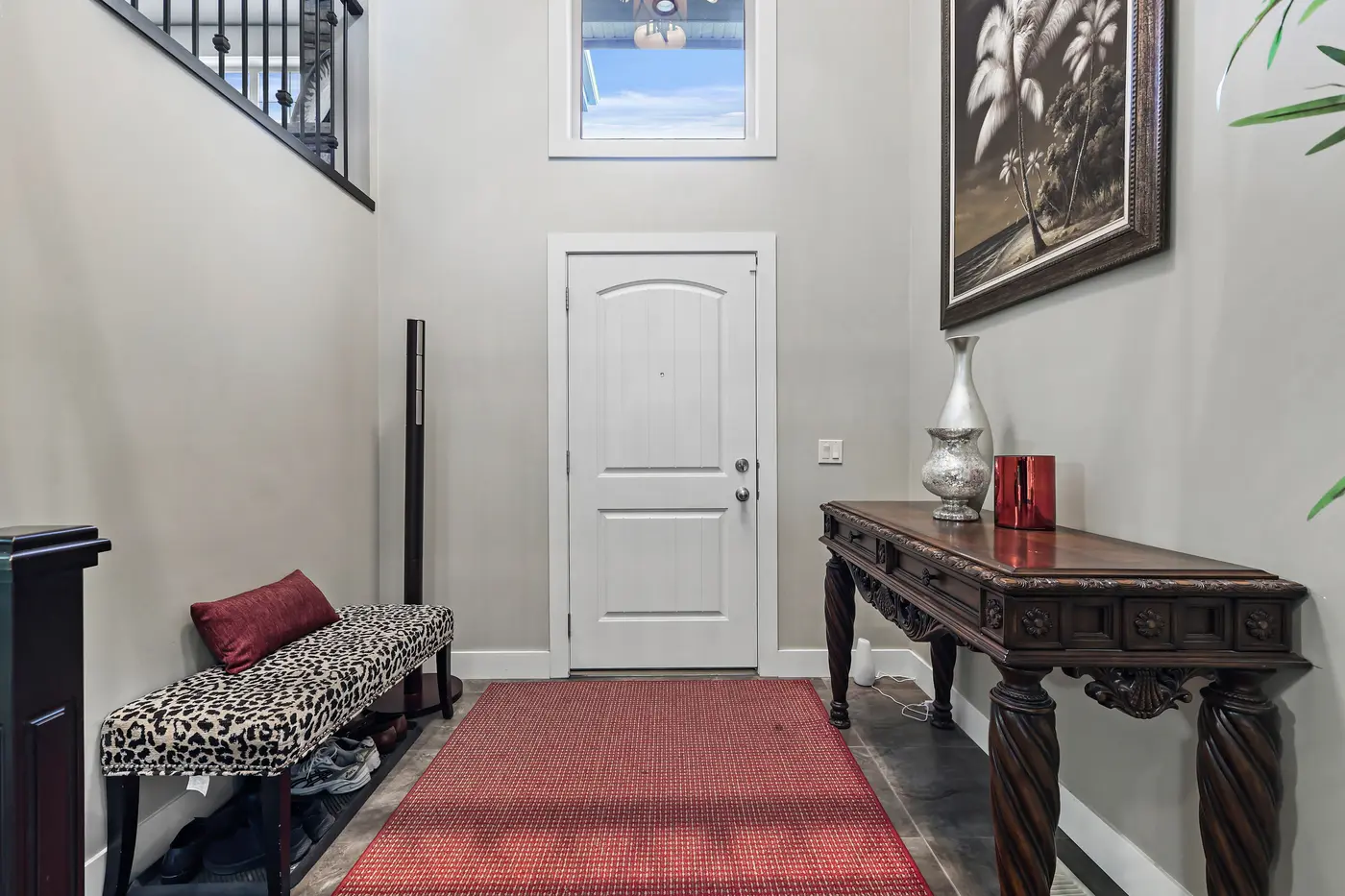 The tall entry foyer, daylight falling from the transom window above the front door onto a red runner, a bench, and a carved console table.