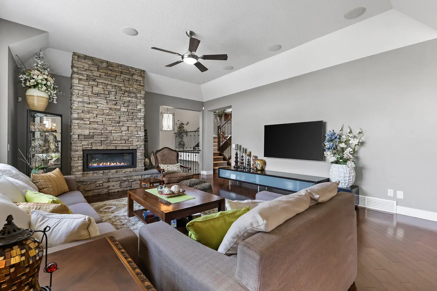 The floor-to-ceiling stacked-stone fireplace in the great room, its linear gas flame lit beneath the mounted television.