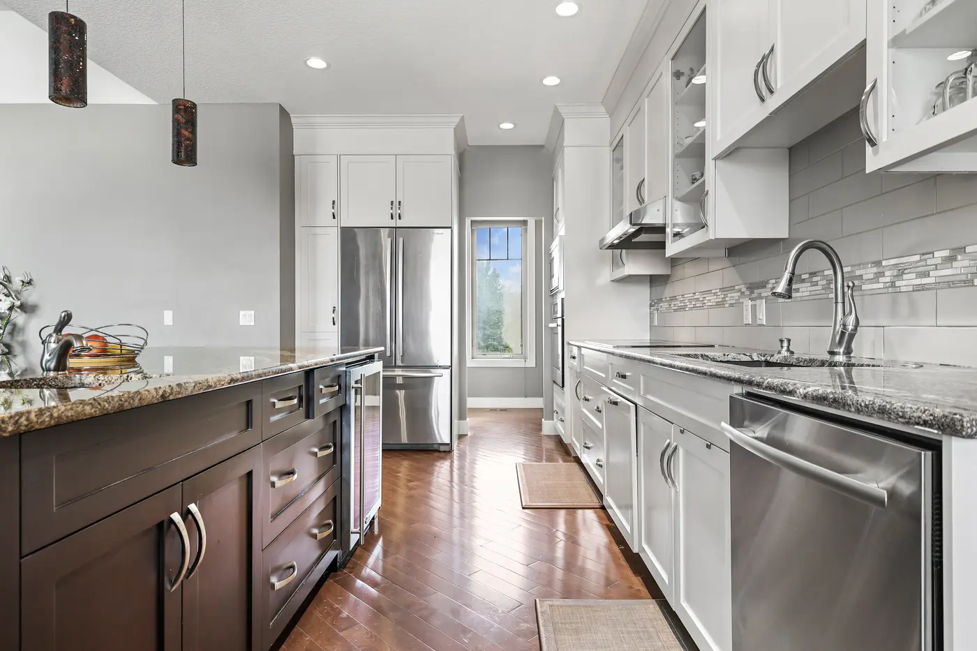 Down the working side of the kitchen — granite counters, stainless dishwasher and French-door refrigerator, and the bar fridge set into the island.