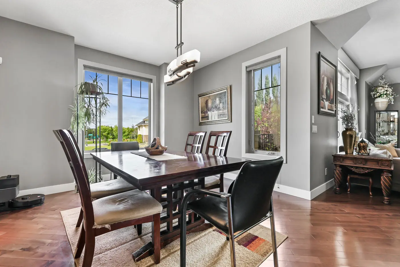 The dining room with windows on two sides, a solid wood table at its centre and the front sitting room beyond.