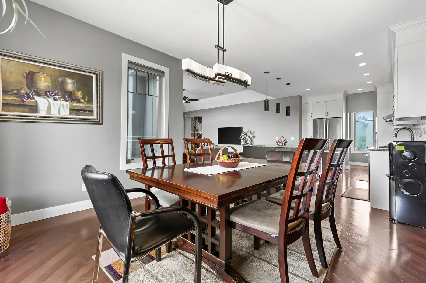 The dining table under its linen-shade chandelier, looking through to the kitchen and the great room television wall.