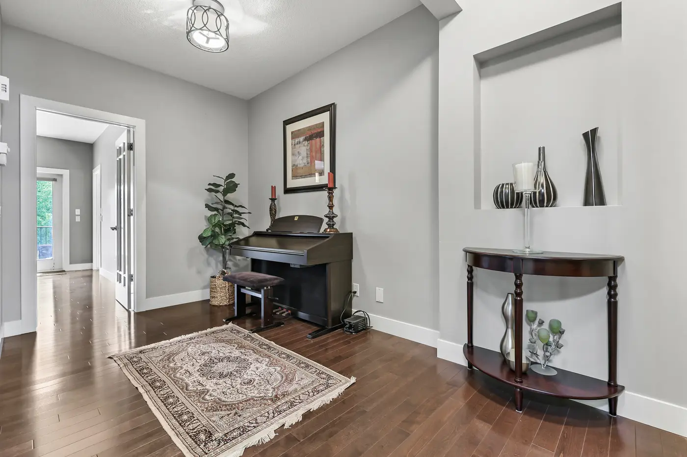 The quiet front sitting room off the foyer, an upright piano and console table under a simple pendant light.