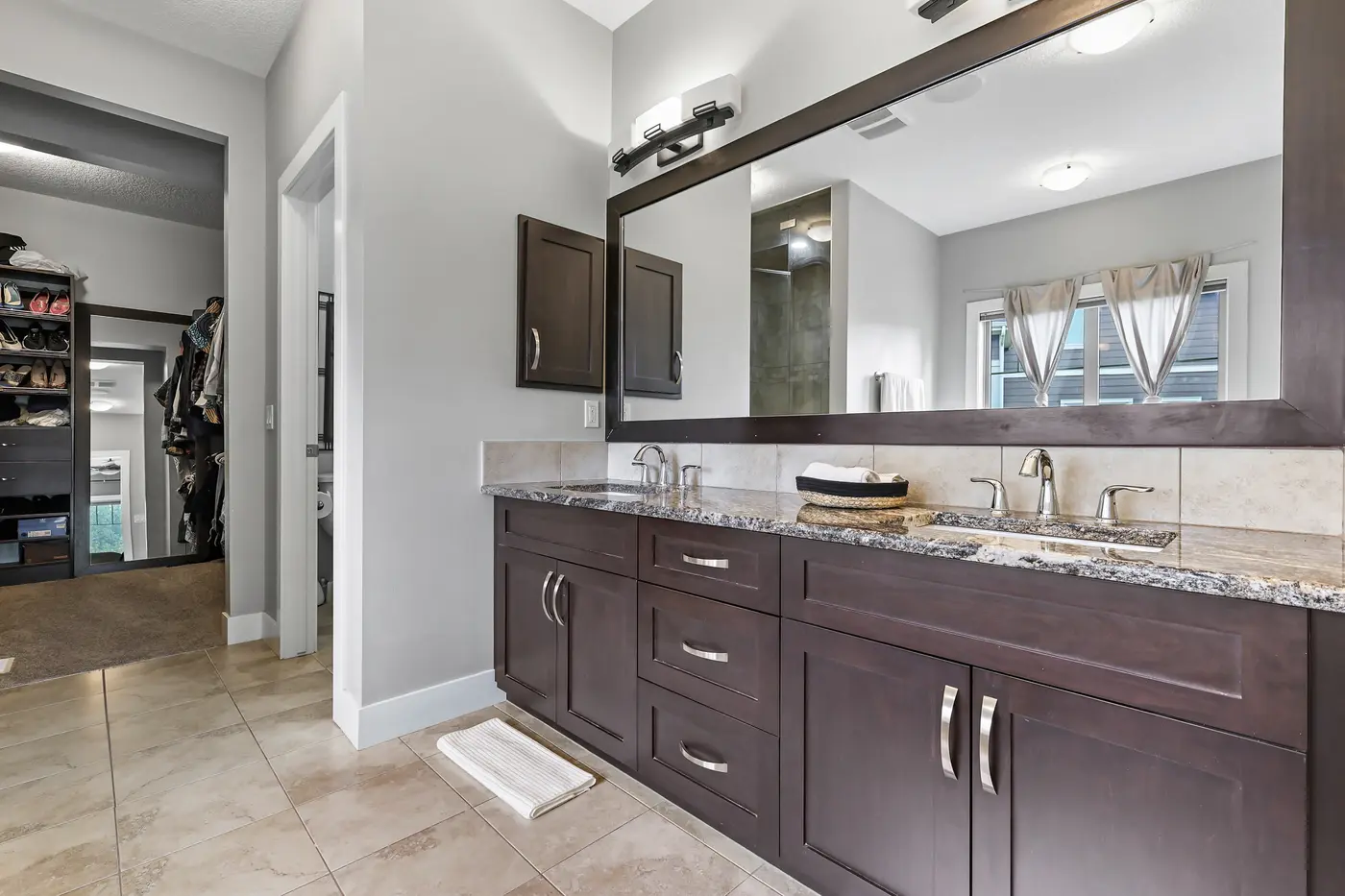The double granite vanity of the ensuite with espresso cabinetry and a full-width mirror, the walk-in closet beyond.