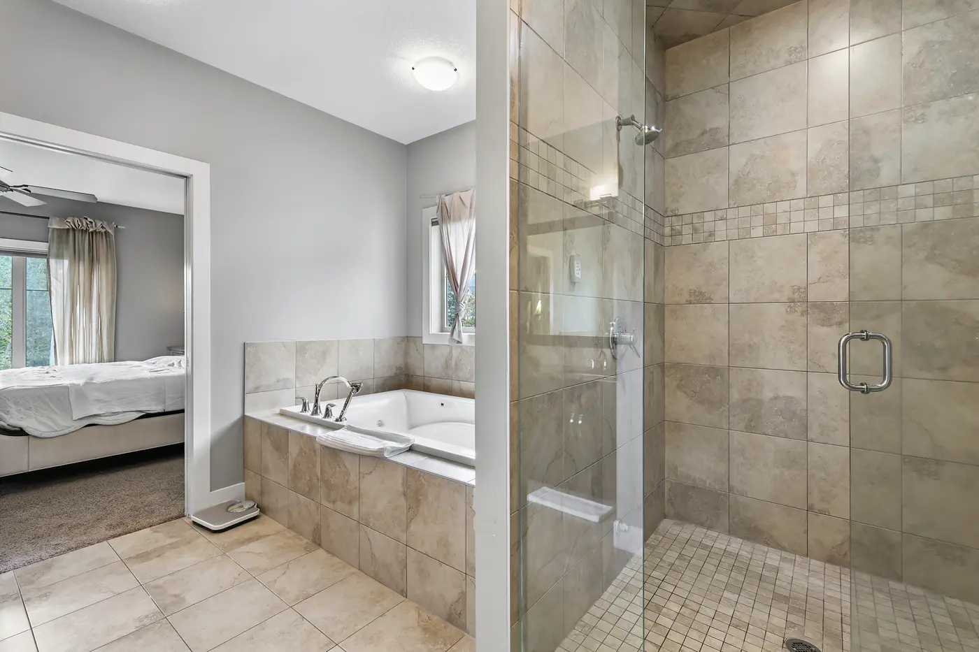 The glass-and-tile walk-in shower beside the corner soaker tub, the primary bedroom just visible through the doorway.
