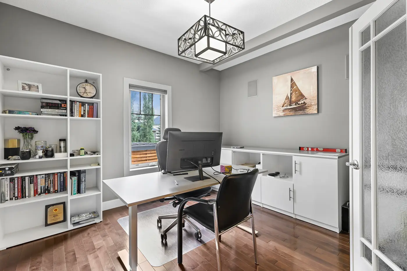 The main-floor den behind French doors — a proper home office with built-in cabinetry, open shelving, and a window to the front street.