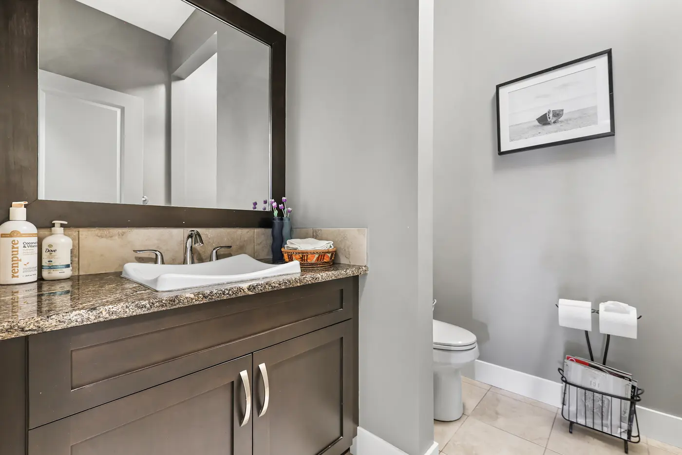 The main-floor powder room, a granite-topped vanity in dark wood with a framed mirror.