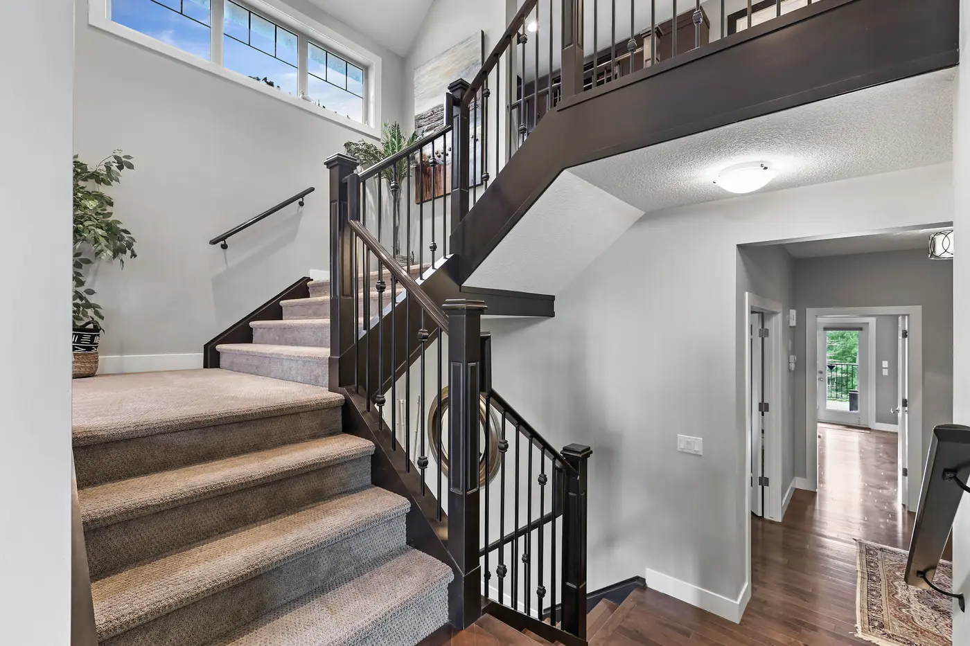 A band of windows lighting the carpeted staircase to the upper floor, with the hall to the main-floor primary retreat beyond.