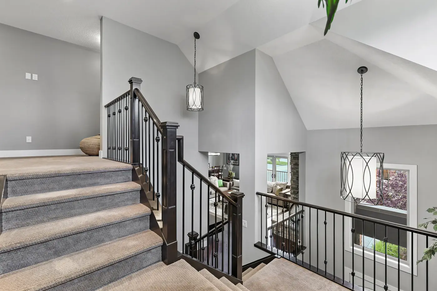 The upper landing under vaulted ceilings, iron-railed and open to the great room and its lantern pendants below.