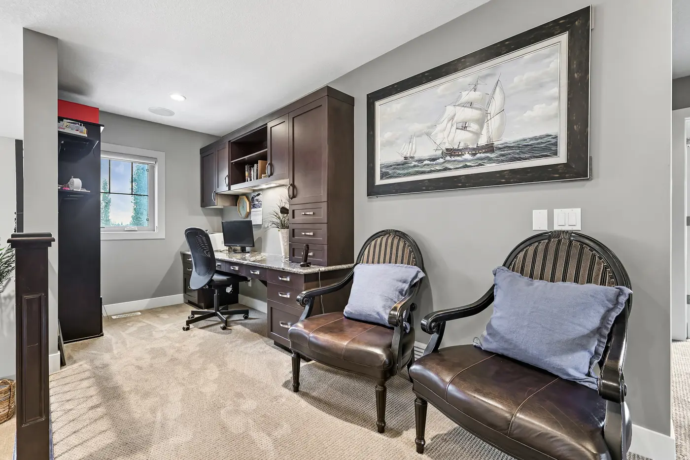 The upstairs flex space — a built-in desk and hutch for homework, two club chairs, and a tall ship painting on the wall.