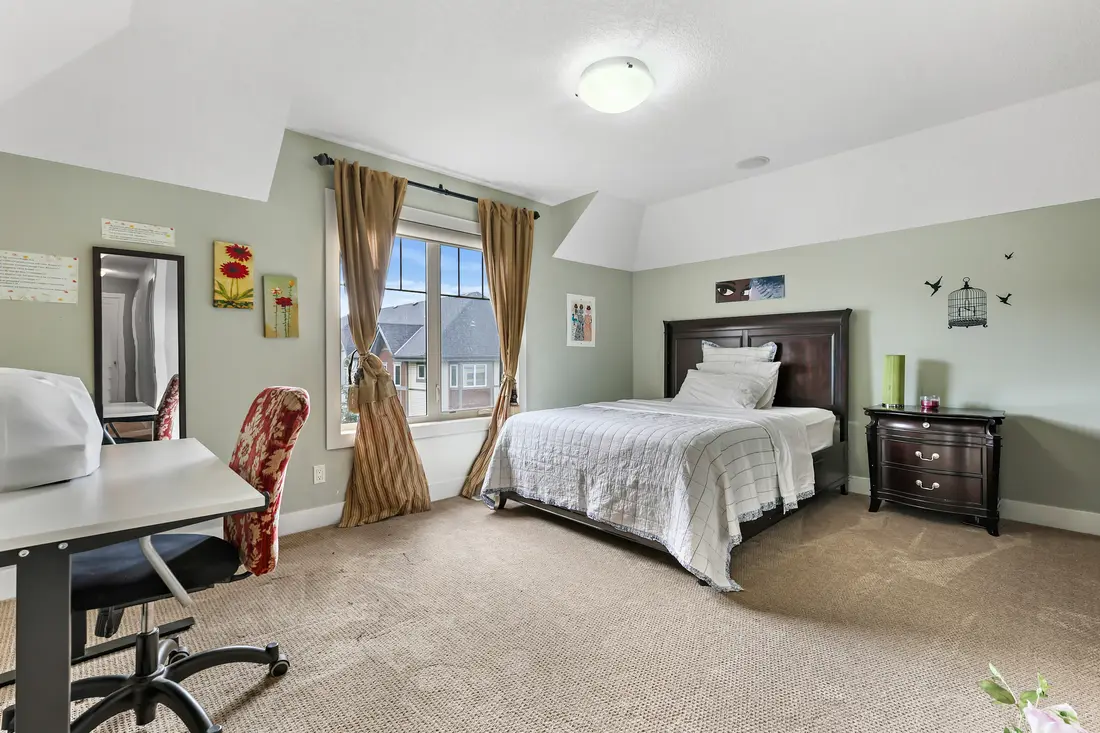 A generous upstairs bedroom with a queen bed, a study desk by the window, and a view over the cul-de-sac.
