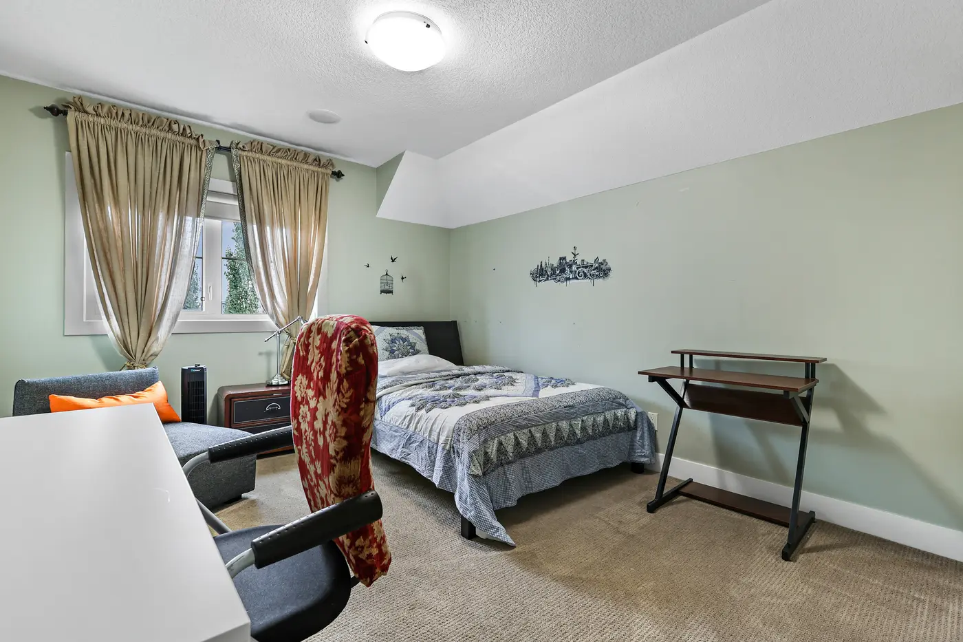 The second upstairs bedroom with a reading chair by the window and a desk in the corner.