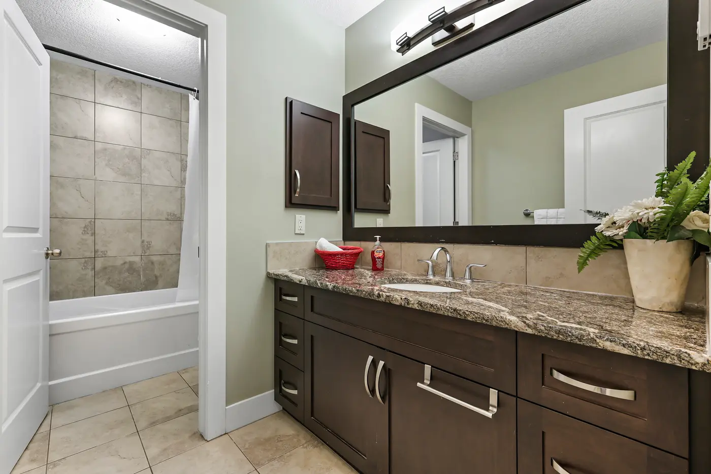 The four-piece upstairs bathroom — granite-topped vanity in dark wood, and a tiled tub-shower beyond the pocket wall.