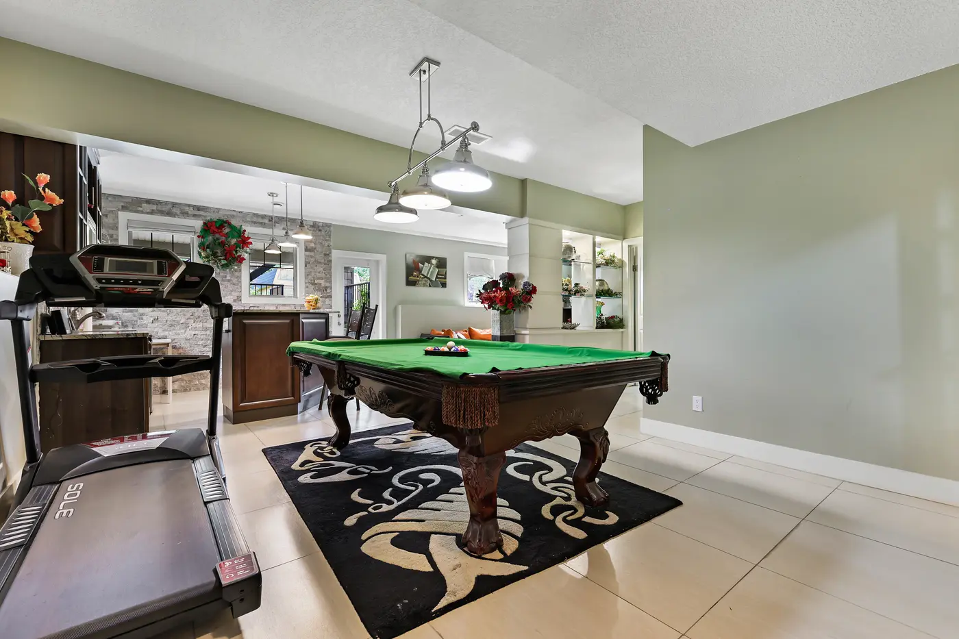 The game room from the family room side, pendant lamps over the billiard table and the bar behind.