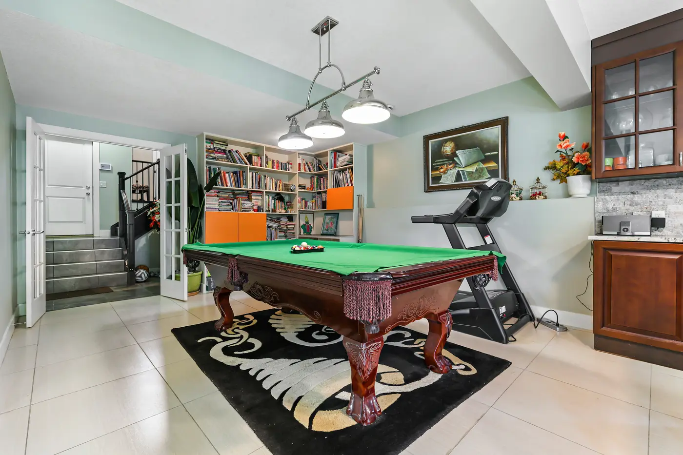 The walkout game room with its library wall of shelves, French doors opening to the lower foyer and stairs.