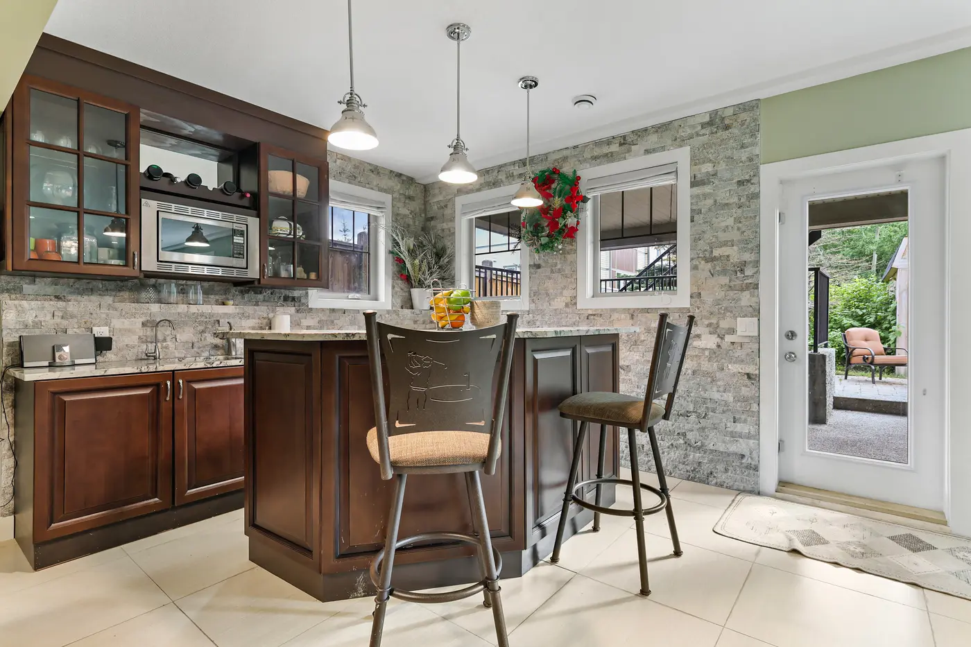 The walkout level’s kitchenette bar against a ledgestone wall — granite counters, bar seating, and its own door to the lower patio.
