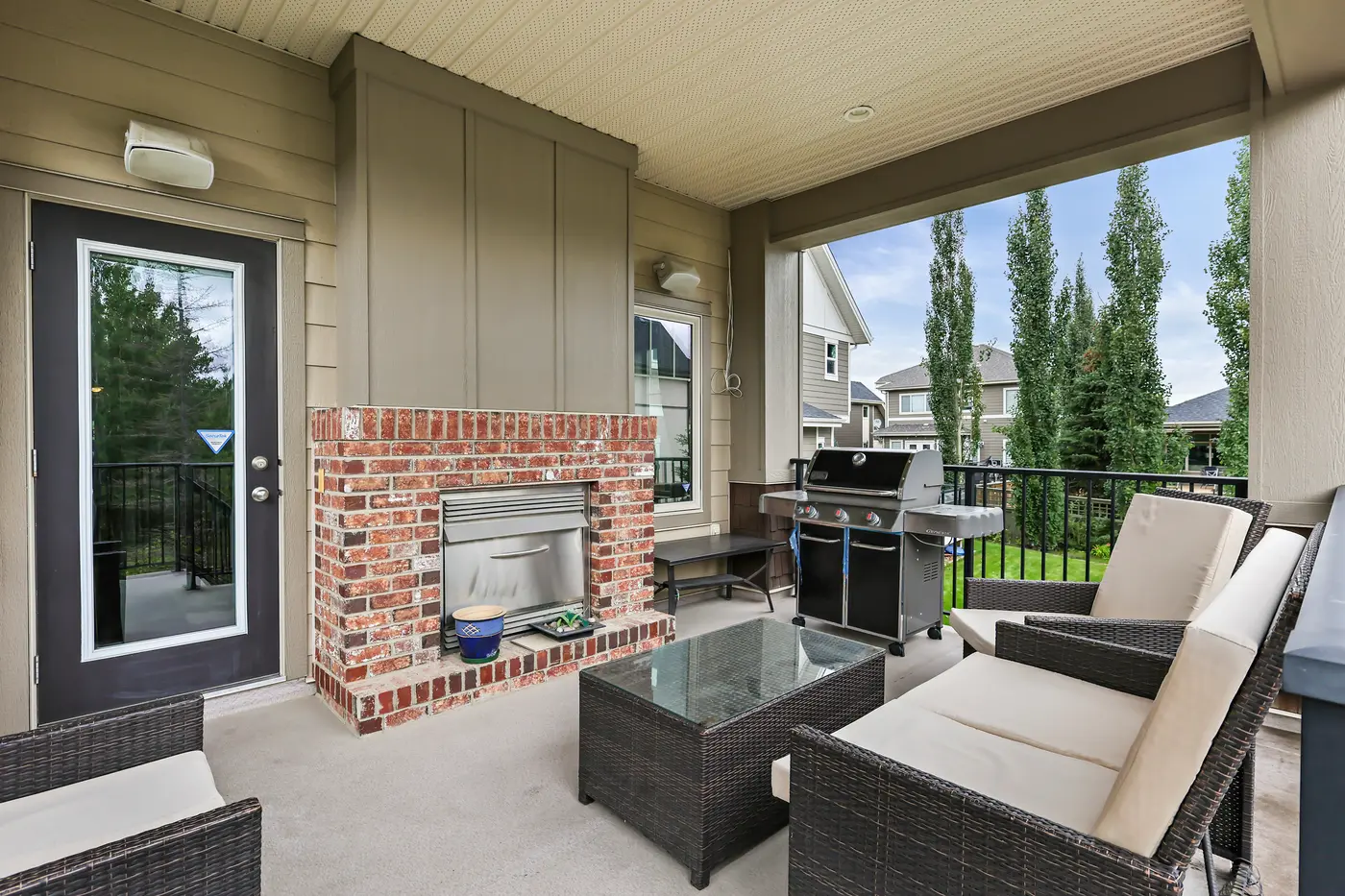 The covered patio in full — brick fireplace, barbecue, and lounge seating under the roof, open to the treed yard.