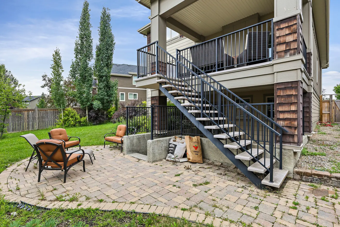The back of the home with its deck staircase descending to a circular paver patio set with lounge chairs.