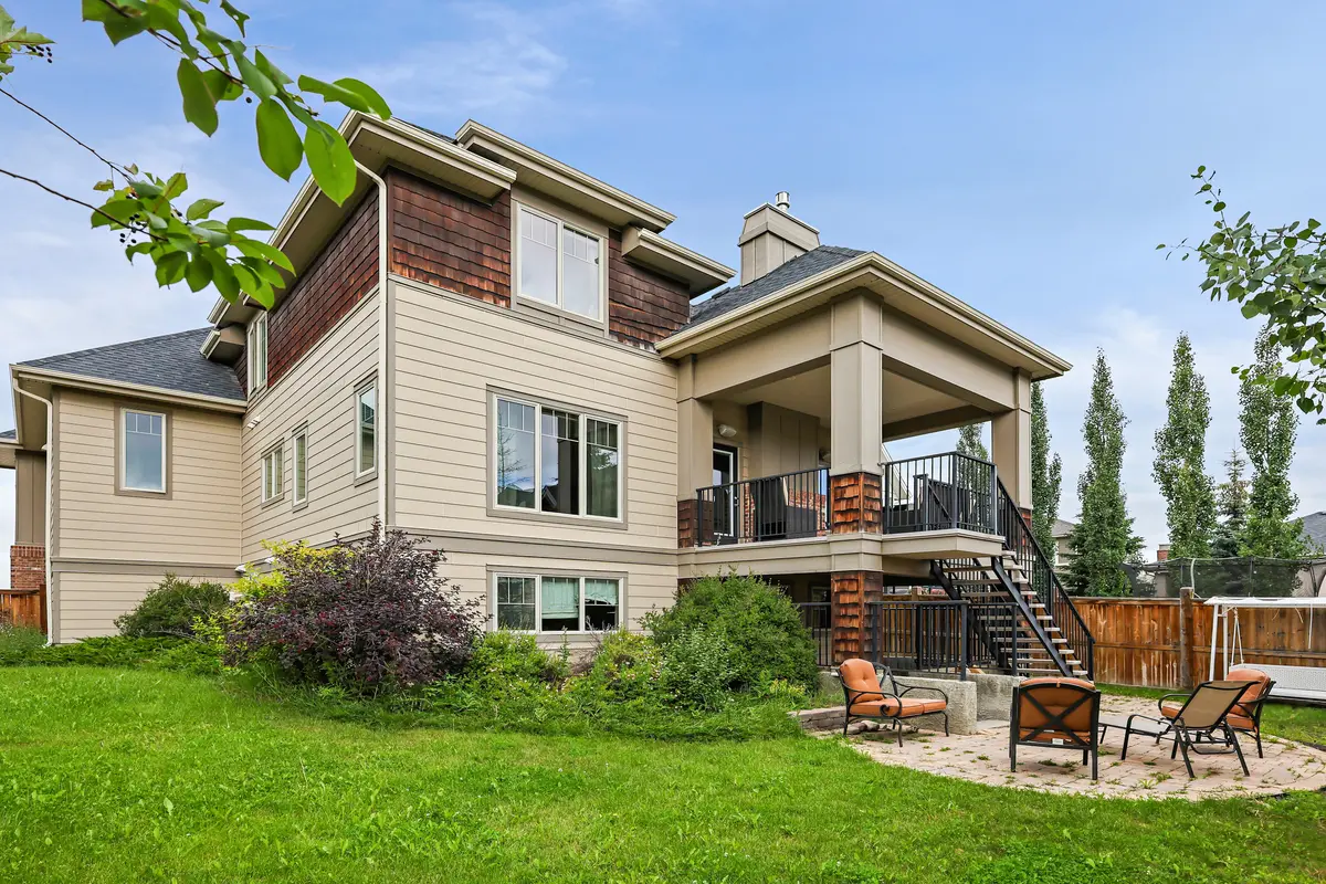 The rear elevation from the lawn — the covered patio on its brick piers, the deck stairs, and the fire-pit patio below.